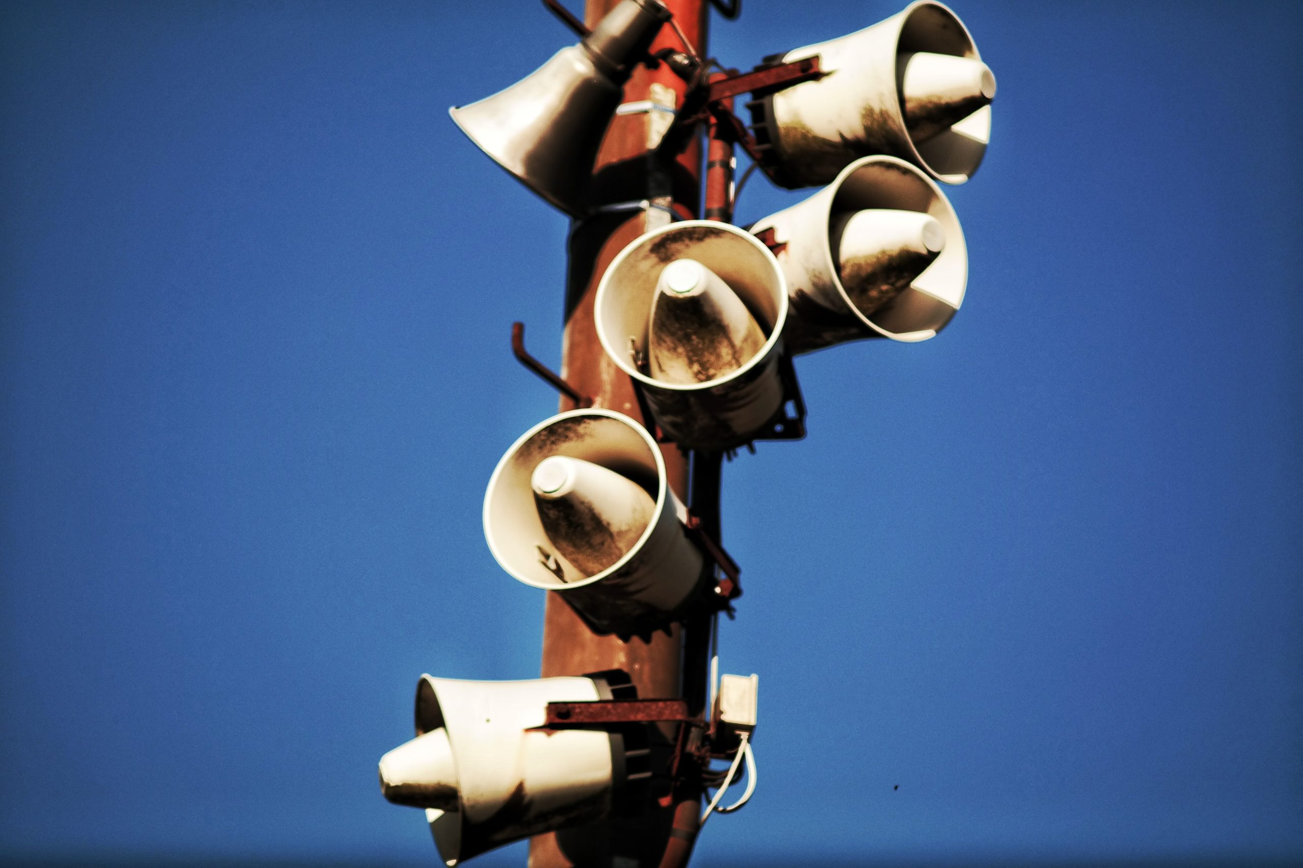 Loudspeakers attached to a pole against a blue sky. Photo by Jens Mahnke from Pexels