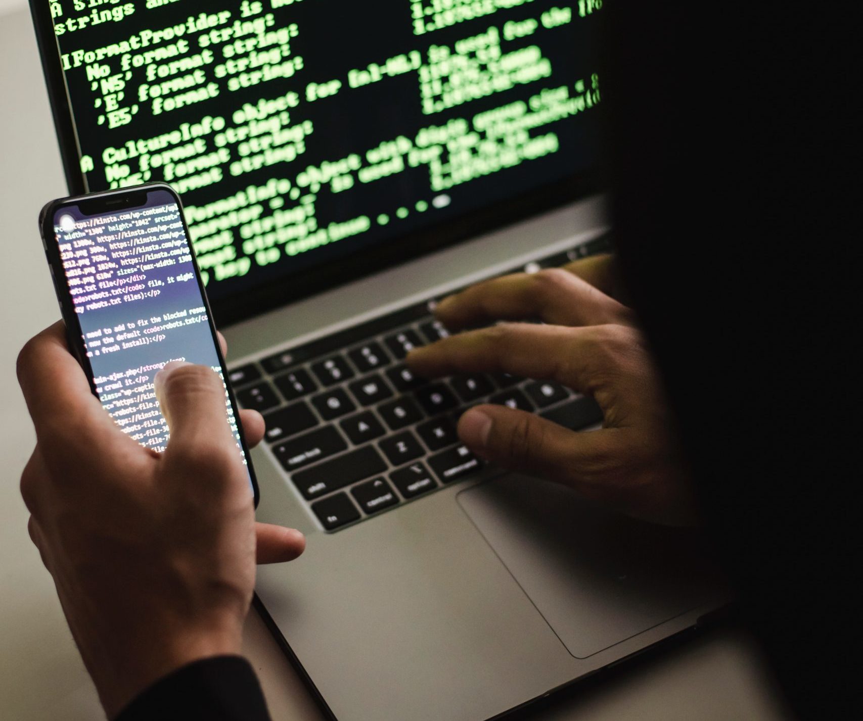 Somebody writing code on a laptop while looking at code on a phone. Photo by Sora Shimazaki from Pexels