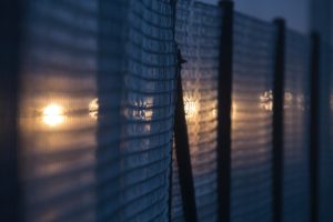 Wire fences at night with lights peaking through. Photo by Phil Botha on Unsplash